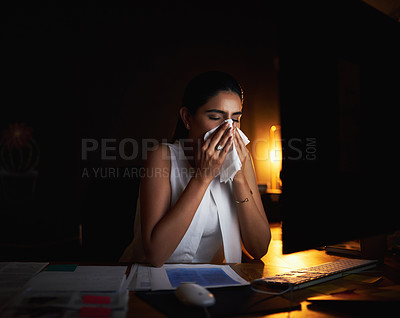 Buy stock photo Shot of a young businesswoman blowing her nose while working late in an office