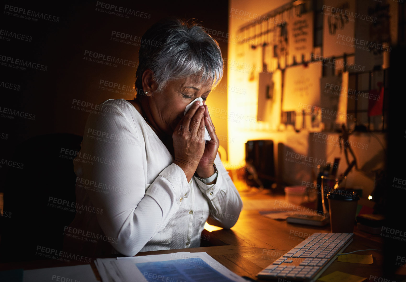 Buy stock photo Shot of a mature businesswoman blowing her nose while working late in an office
