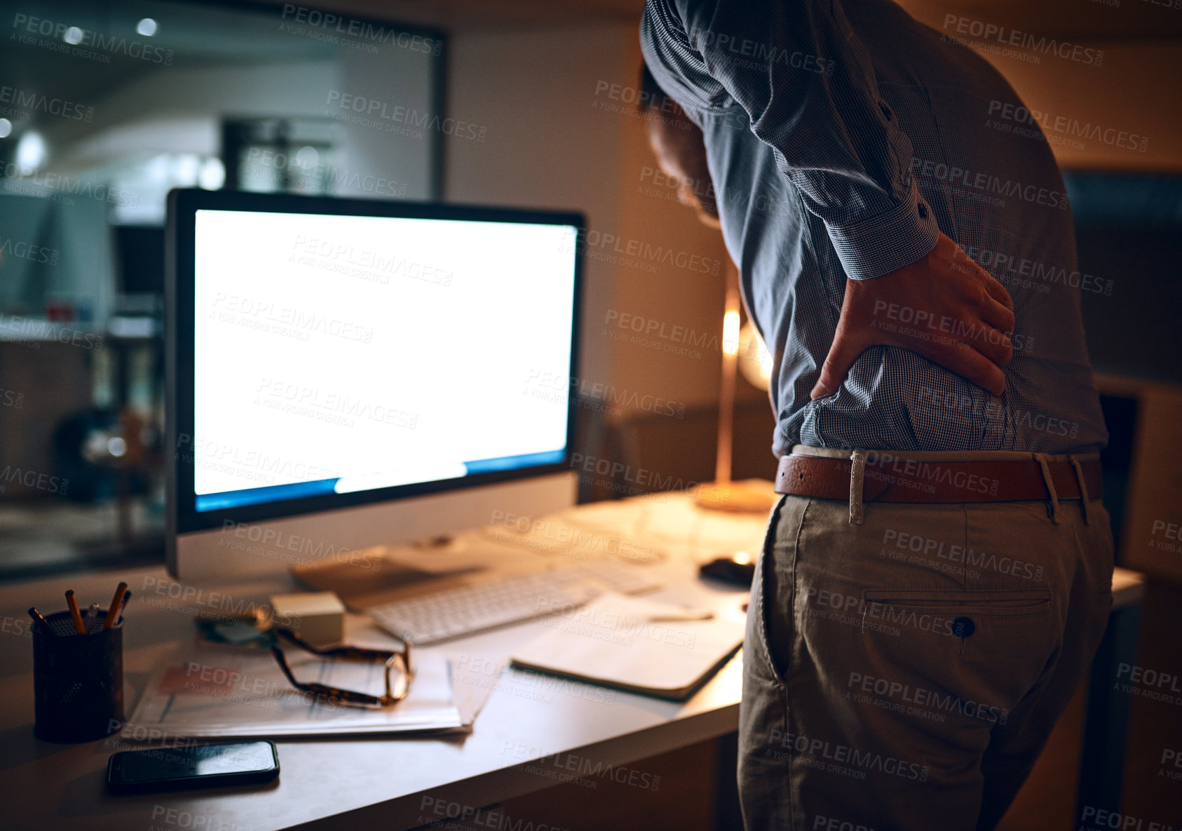 Buy stock photo Rear view shot of a young businessman suffering with back pain while working late in an office