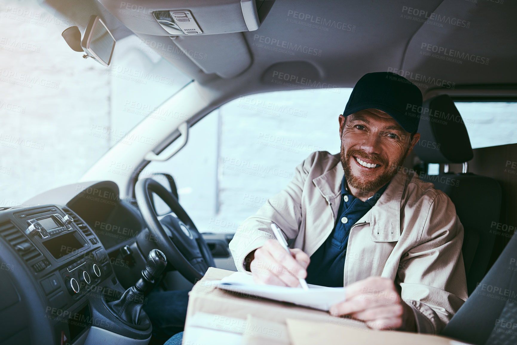 Buy stock photo Portrait of a cheerful young delivery man seated in his car with boxes while signing on a digital tablet during the day