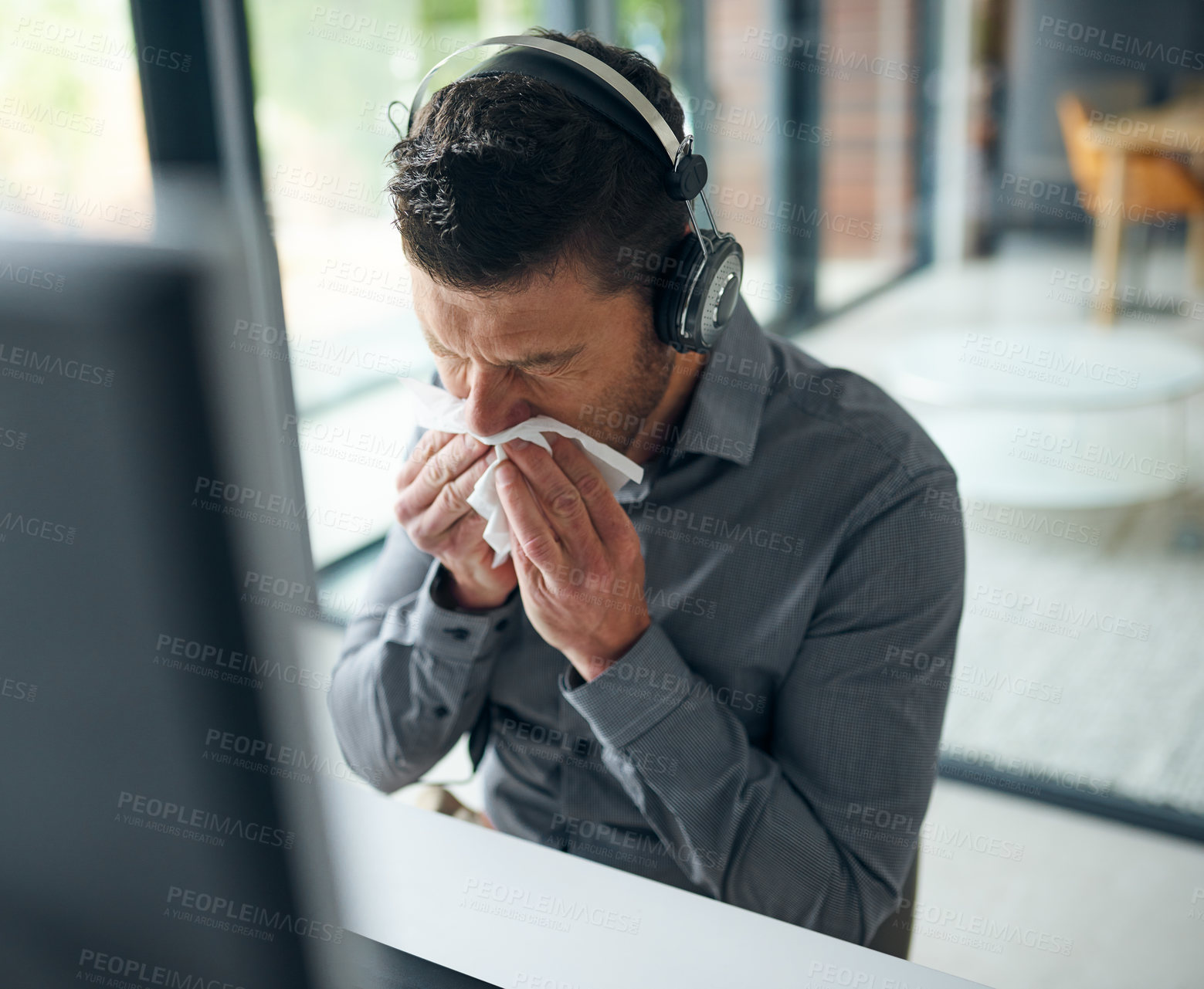 Buy stock photo Shot of a mature man blowing his nose while working on a computer in a call centre