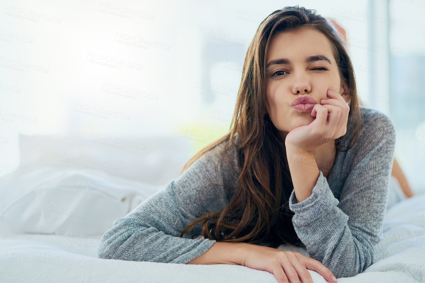 Buy stock photo Portrait of an attractive young woman blowing a kiss while lying in bed at home during the day