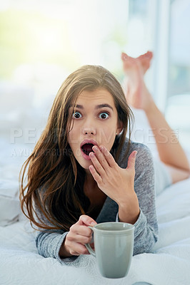 Buy stock photo Portrait of an surprised looking young woman drinking coffee while lying on her bed at home during the day