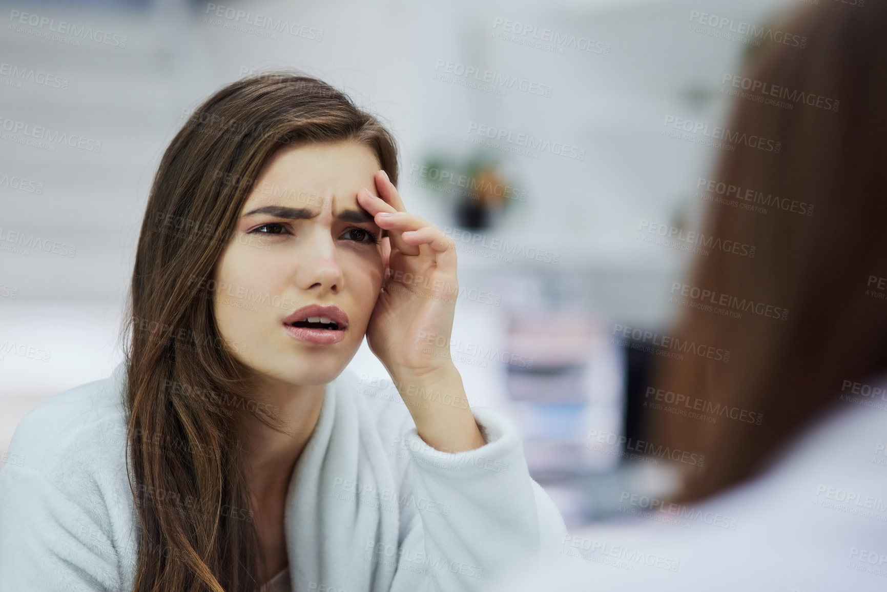 Buy stock photo Shot of a confused looking young woman looking into a mirror with her hand touching her face at home during the day