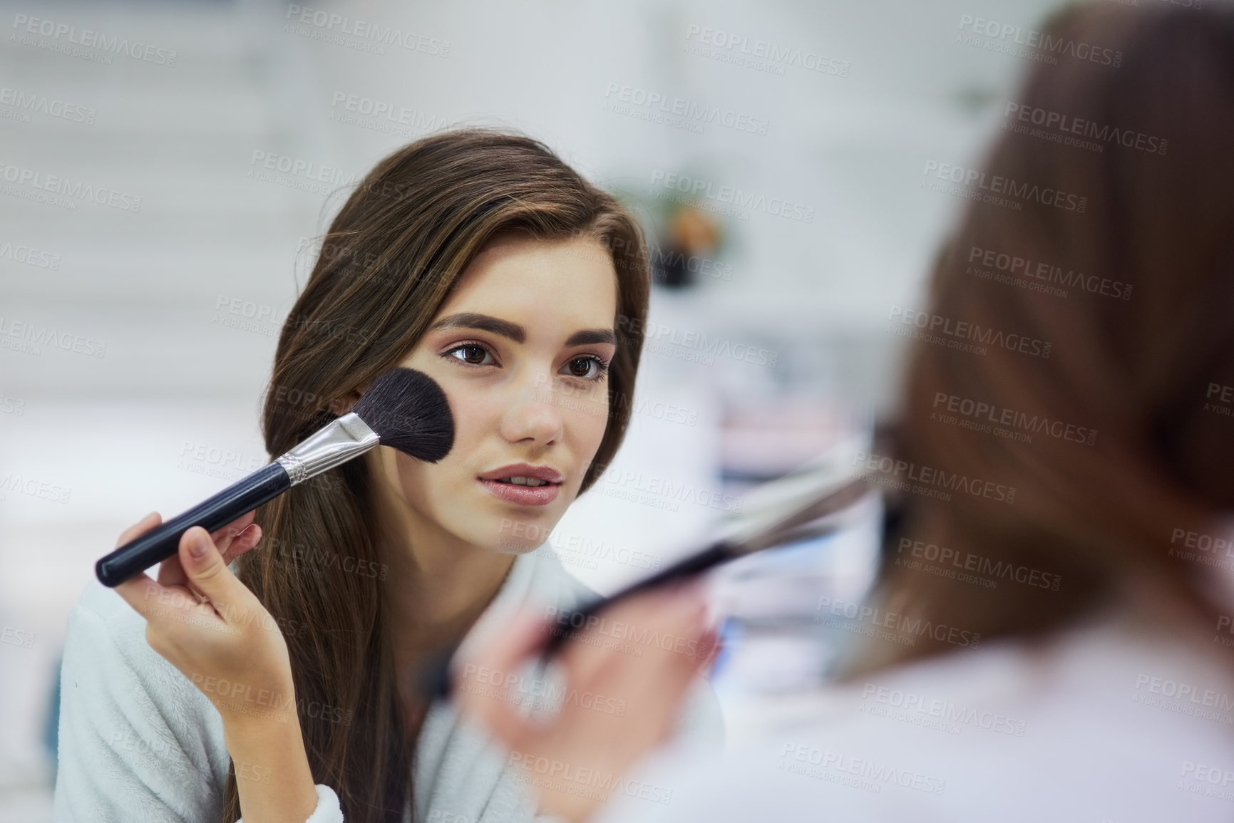 Buy stock photo Shot of an attractive young woman looking into a mirror while applying makeup to her face at home during the day