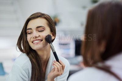 Buy stock photo Shot of an attractive young woman looking into a mirror while applying makeup to her face at home during the day