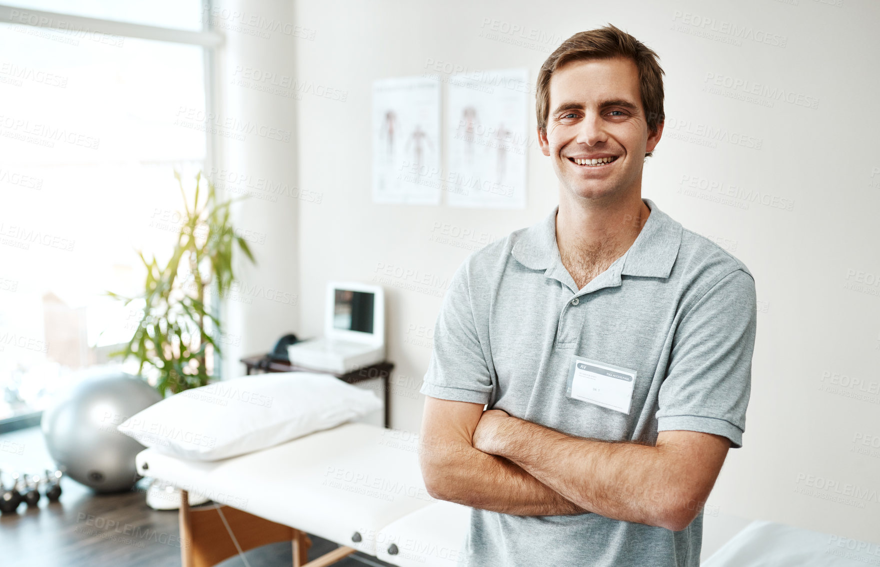 Buy stock photo Portrait of a confident young male physiotherapist standing with his arms folded inside of his office