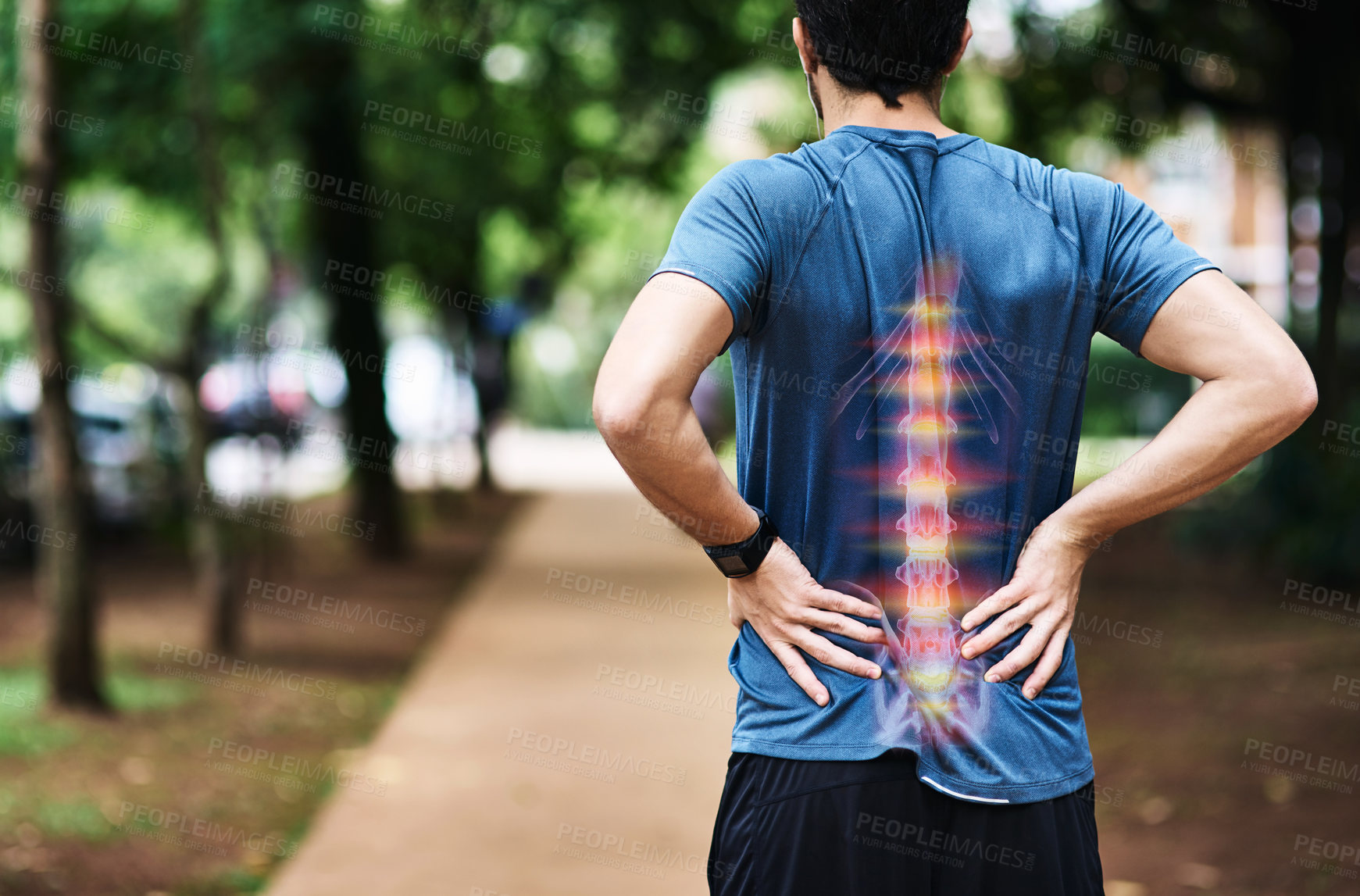 Buy stock photo Rear view shot of a sporty young man holding his back in pain while exercising outdoors