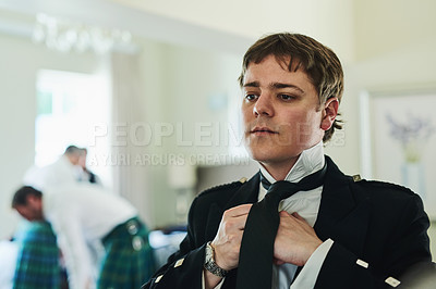 Buy stock photo Shot of a confident young man folding a tie while looking into a mirror to get ready for a wedding