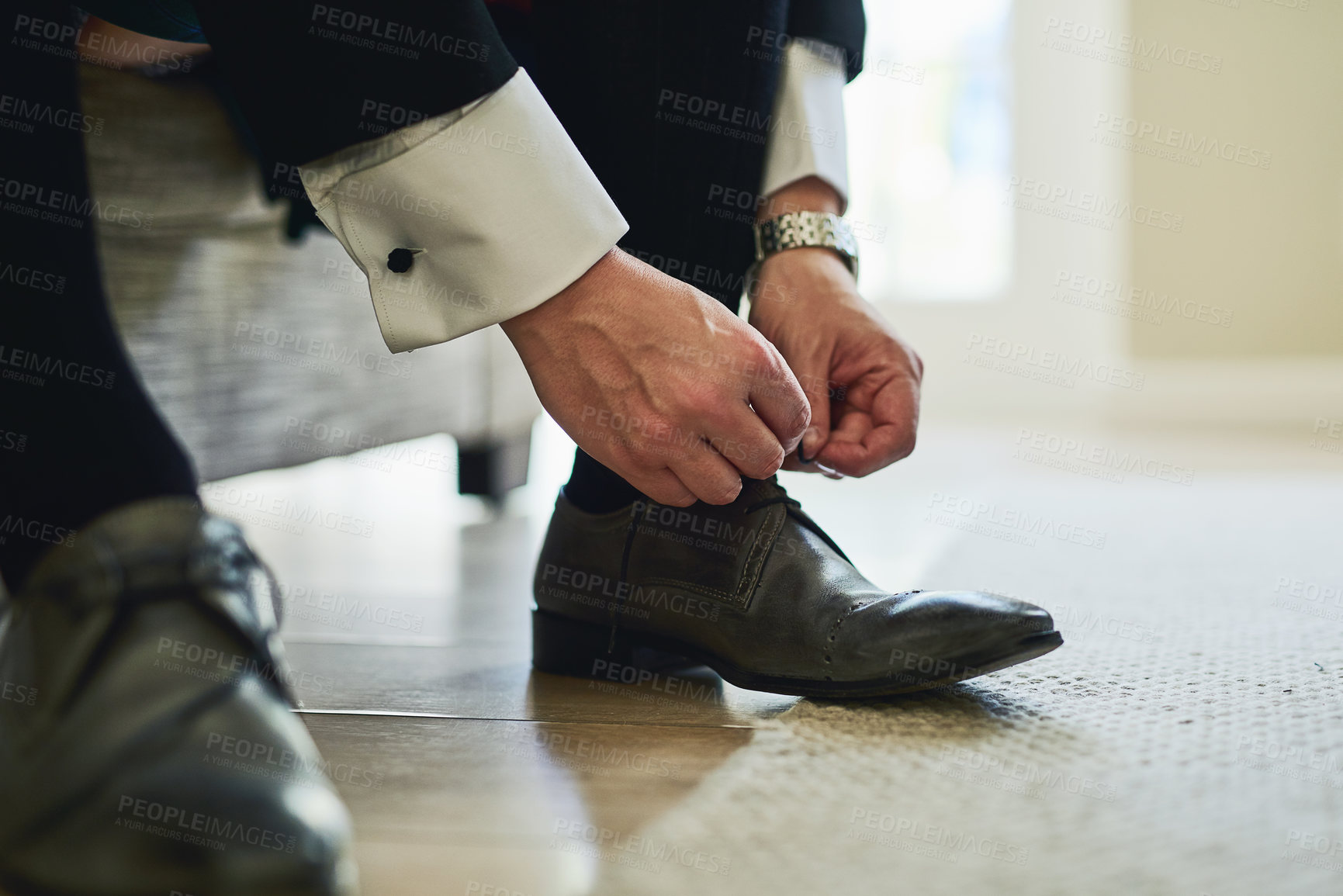 Buy stock photo Shot of a unrecognizable man's hands tying the laces on a pair of formal shoes inside a building during the day