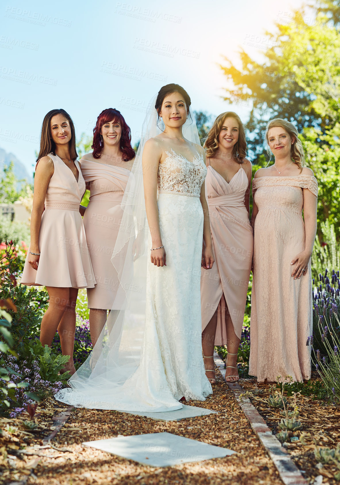 Buy stock photo Portrait of a cheerful young bride and her bride's maids standing together outside during the day