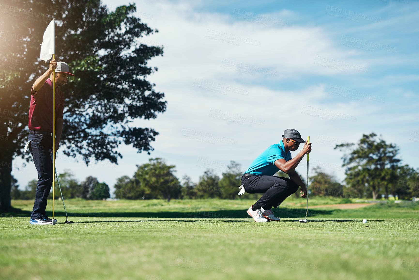 Buy stock photo Shot of a focused young male golfer looking at a golf ball while being seated on the grass outside during the day