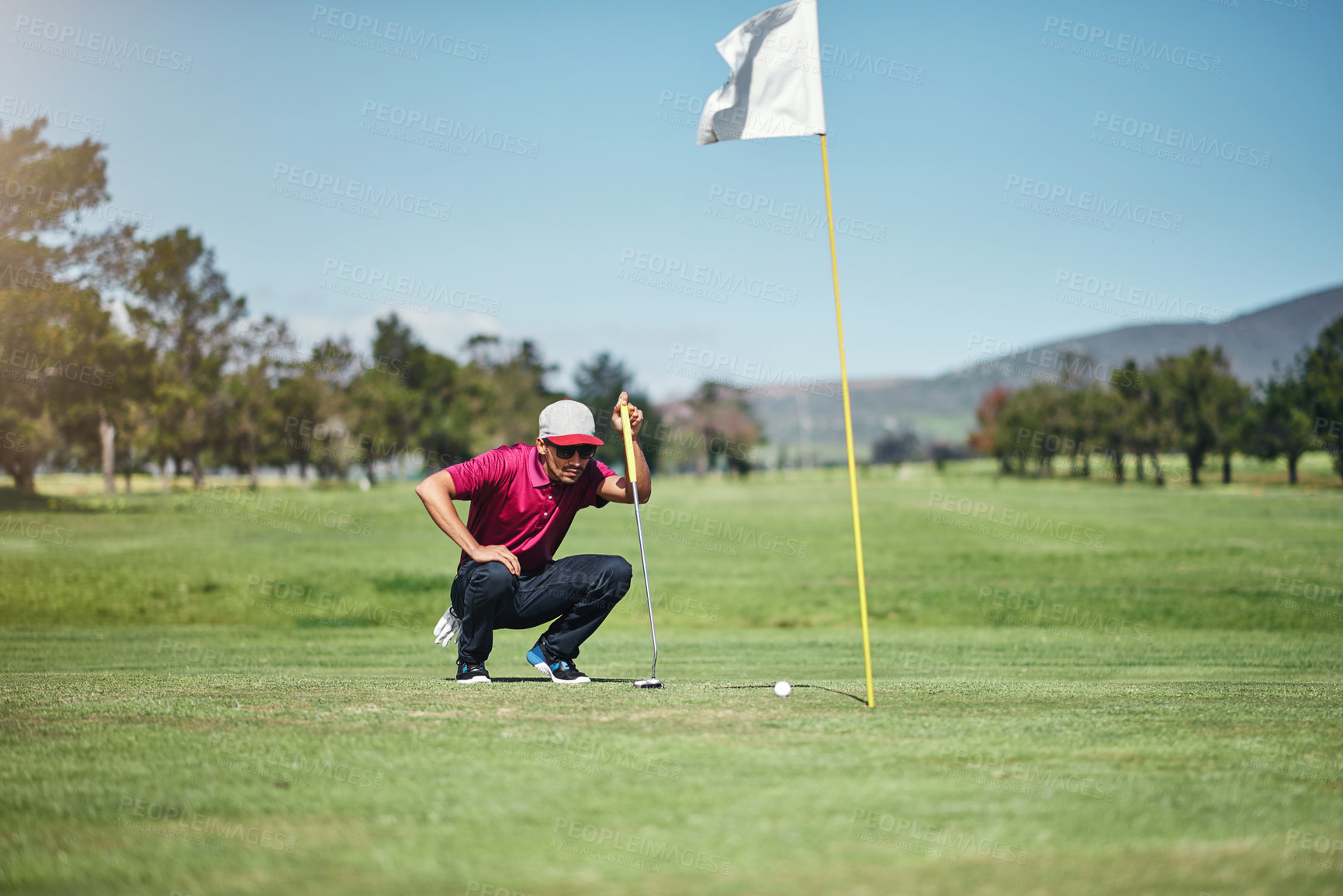 Buy stock photo Shot of a focused young male golfer looking at a golf ball while being seated on the grass outside during the day