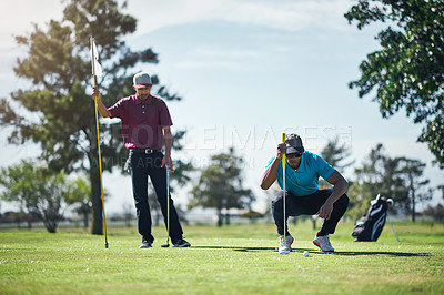 Buy stock photo Shot of a focused young male golfer looking at a golf ball while being seated on the grass outside during the day