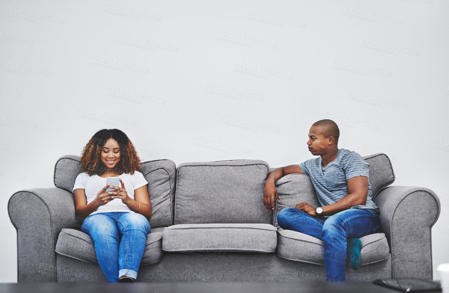 Buy stock photo Shot of a young woman texting on a cellphone while her boyfriend watches in anger