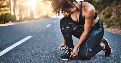 Buy stock photo Shot of a sporty young woman tying her shoelaces before her run