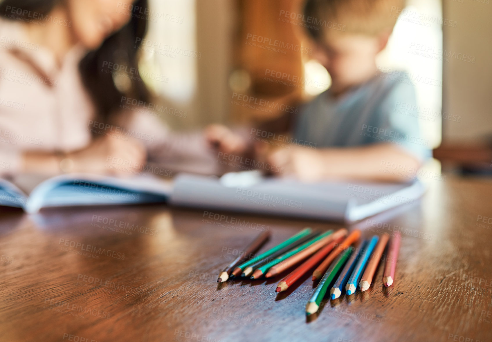 Buy stock photo Shot of pencils on a table with a mother and son doing homework in the background