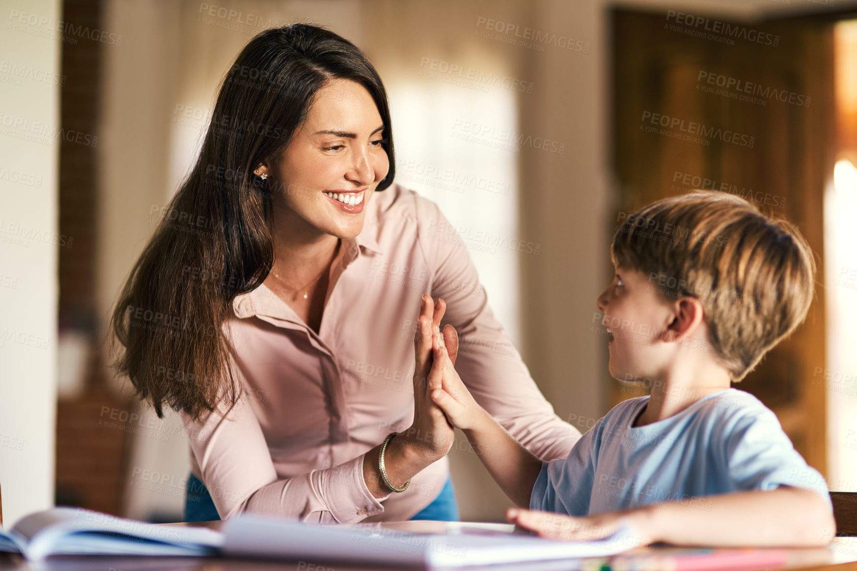 Buy stock photo Shot of a mother giving her son a high five while helping him with his homework