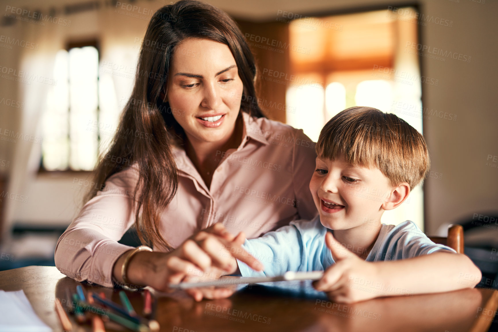 Buy stock photo Shot of a little boy using a digital tablet while doing homework with help from his mother
