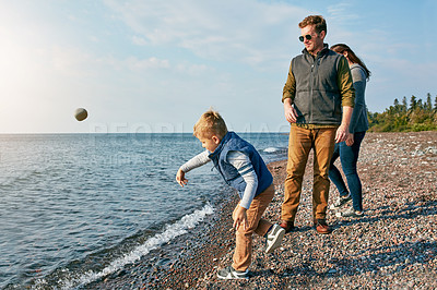 Buy stock photo Shot of a little boy throwing a rock into the lake while his parents watch him