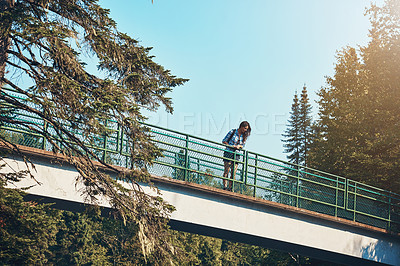 Buy stock photo Shot of an attractive young woman standing on a bridge surrounded by nature