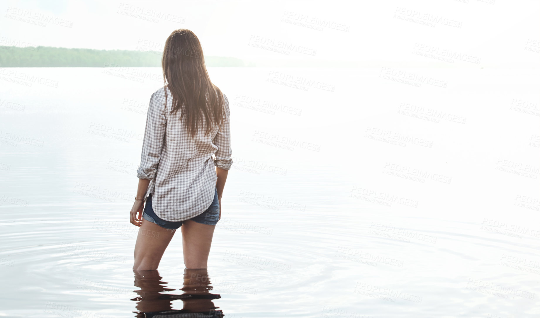 Buy stock photo Rearview shot of a young woman standing in a lake