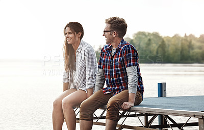 Buy stock photo Shot of a happy young couple sitting on a pier