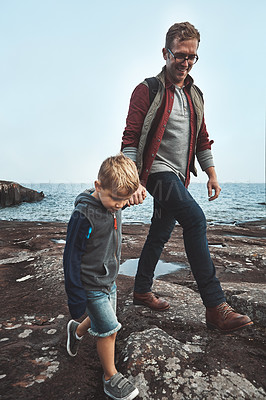 Buy stock photo Shot of a cheerful father and son holding hands while walking next to the ocean outside during the day