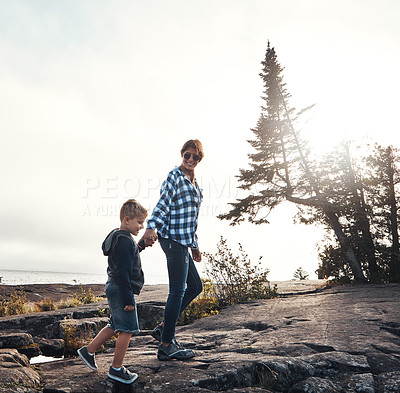 Buy stock photo Shot of a cheerful mother and son holding hands while walking outside in nature during the day