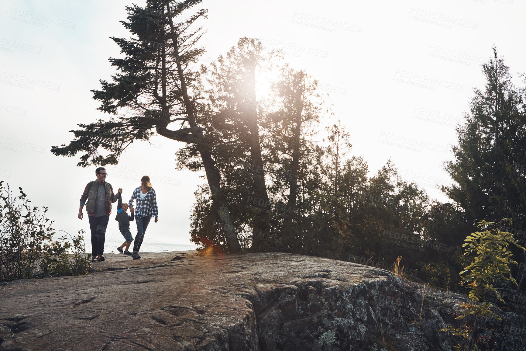 Buy stock photo Wide shot of a cheerful young family holding hands and walking together down a hill outside during the day