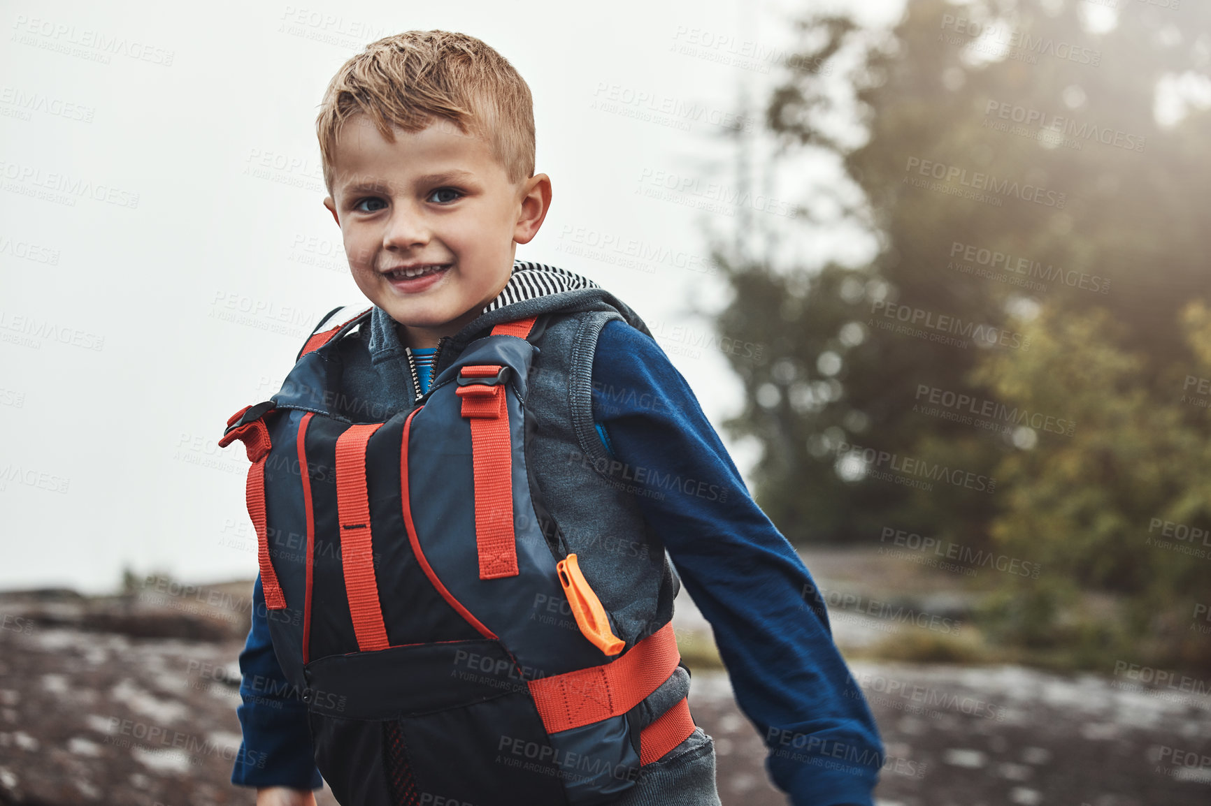 Buy stock photo Portrait of a cheerful little boy wearing a lifejacket while looking at the camera outside during the day