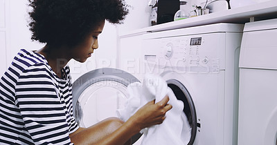 Buy stock photo Shot of a focused young woman putting in clothes in the washing machine to get washed at home during the day