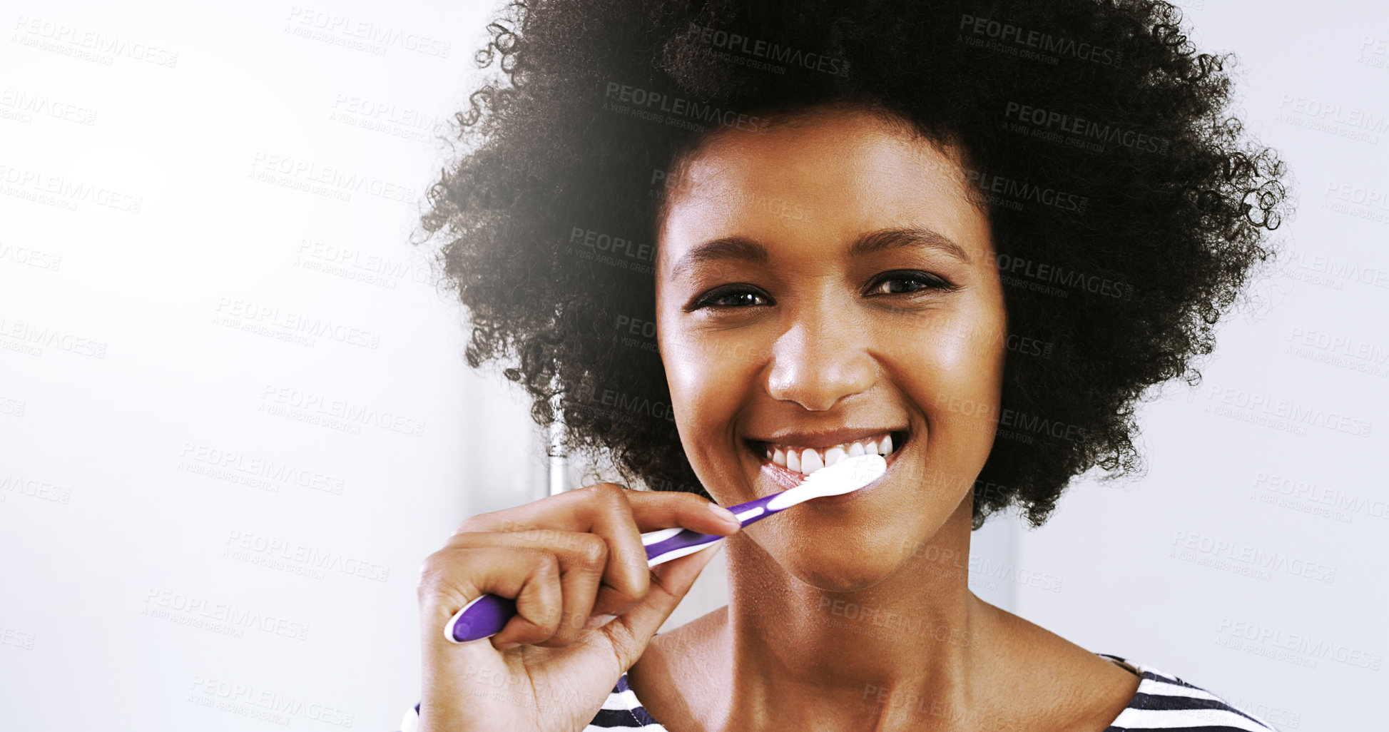Buy stock photo Portrait of a cheerful young woman brushing her teeth while looking at her reflexion in the mirror in the bathroom at home