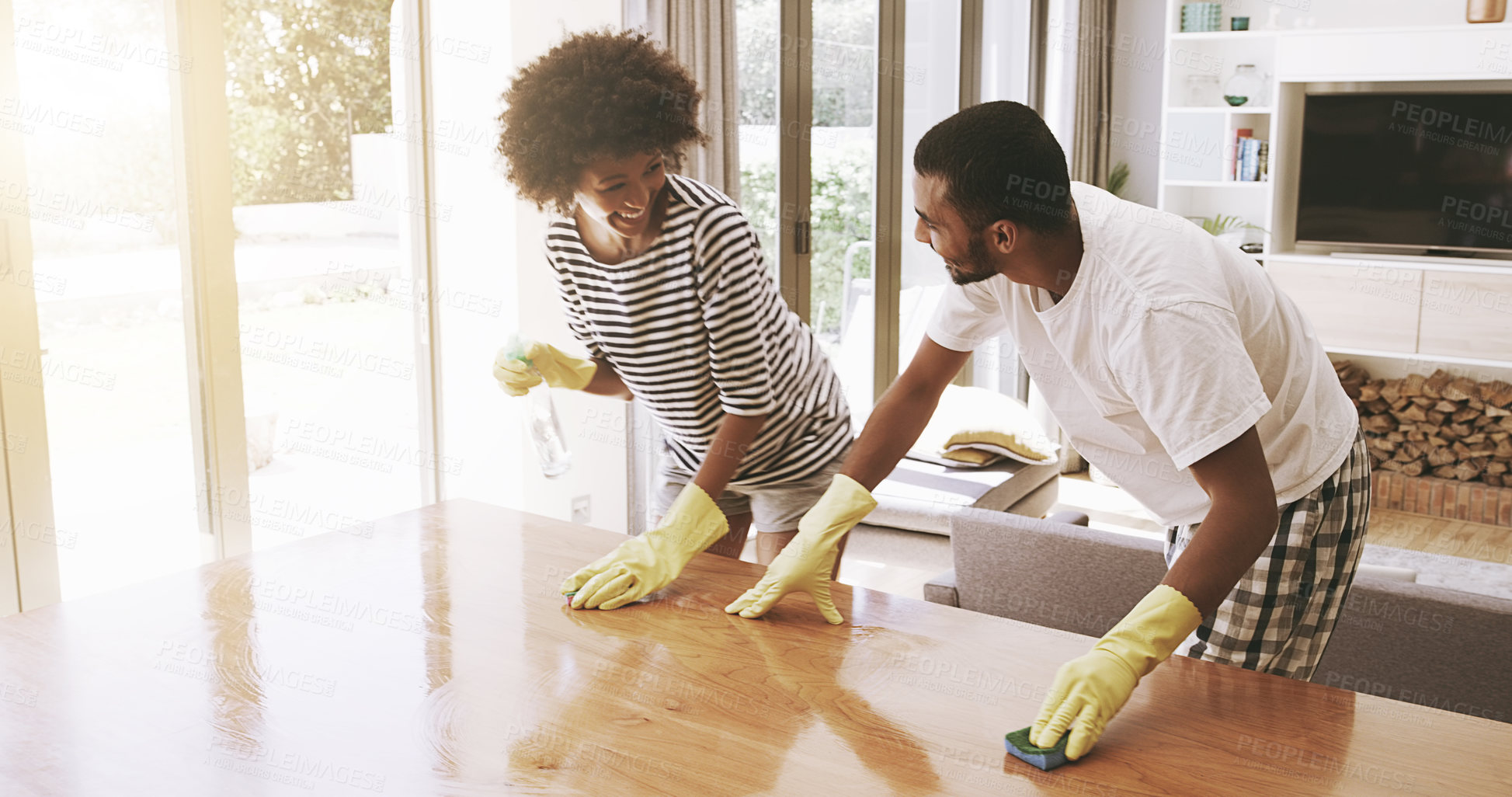 Buy stock photo Shot of a cheerful young couple cleaning the surface of a table with cleaning equipment together at home