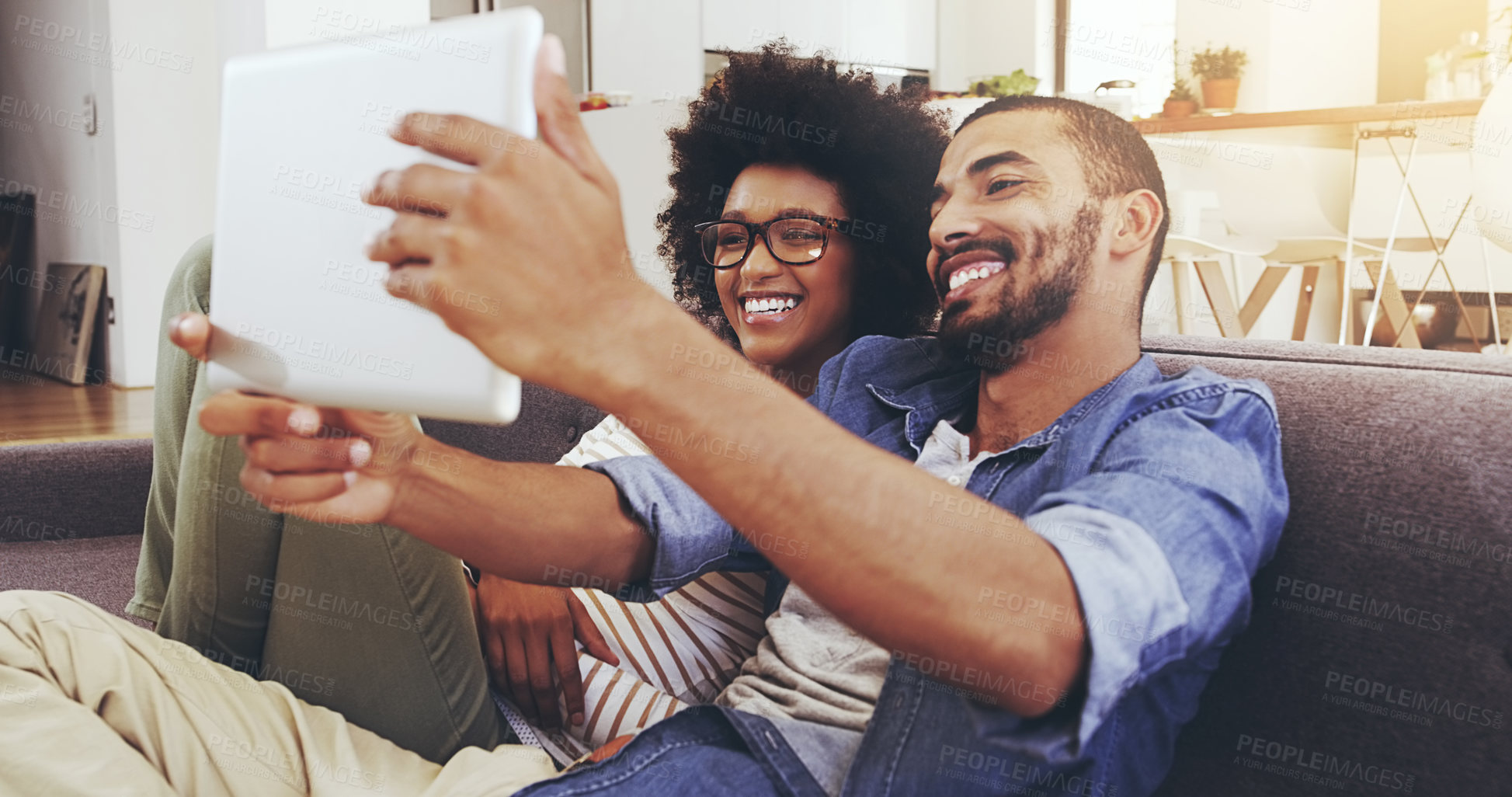 Buy stock photo Shot of a cheerful young couple seated on a couch while taking a self portrait with a digital tablet in the living room at home