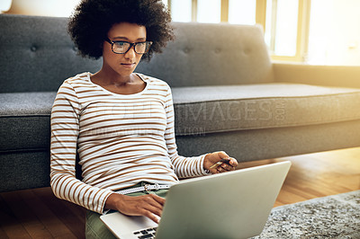 Buy stock photo Shot of a focused young woman doing online banking with her laptop while being seated on the floor next to a couch at home