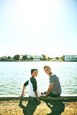 Buy stock photo Full length portrait of two young brothers sitting outside by a lagoon