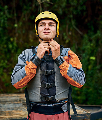 Buy stock photo Shot of a determined young man putting on a protective helmet and getting ready to go river rafting outside during the day