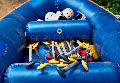Buy stock photo Shot of a a bunch of river rafting equipment lying on top of each other inside of a rubber bout outside during the day