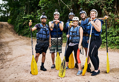 Buy stock photo Portrait of a group of cheerful young people standing together while wearing life jackets and holding rowing paddles outside during the day