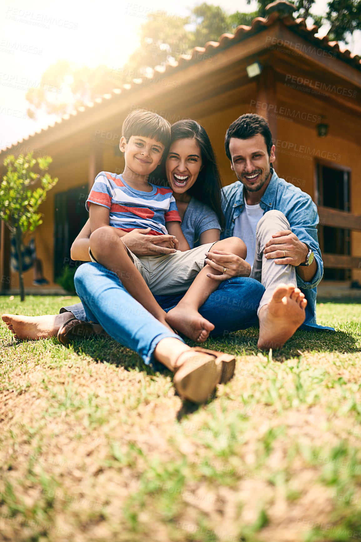 Buy stock photo Full length portrait of a happy young family of three sitting on their lawn in the backyard