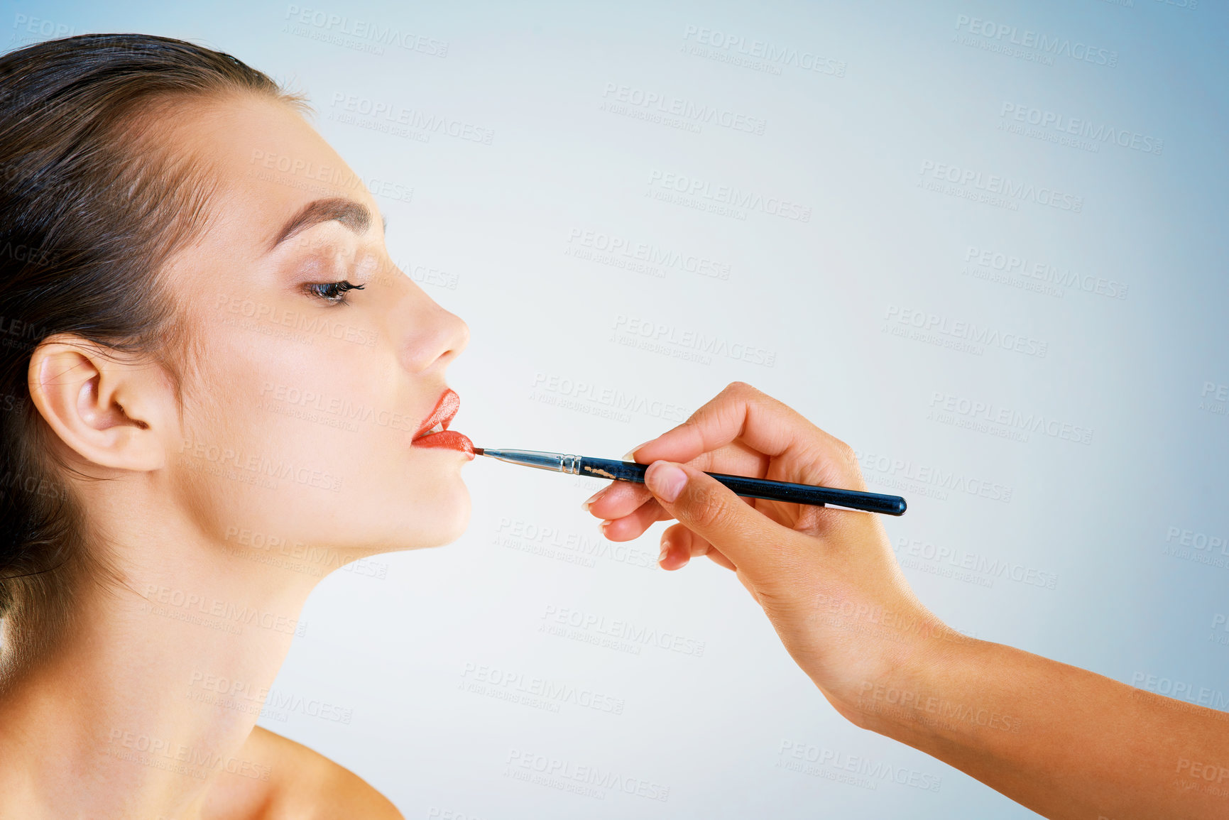 Buy stock photo Cropped studio shot of a hand applying lipstick to beautiful young woman with a brush against a blue background