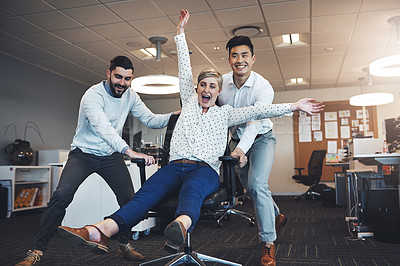 Buy stock photo Shot of businesspeople having fun by taking their colleague for a ride in her chair in the office