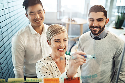 Buy stock photo Shot of businesspeople brainstorming with sticky notes on a glass wall in the office