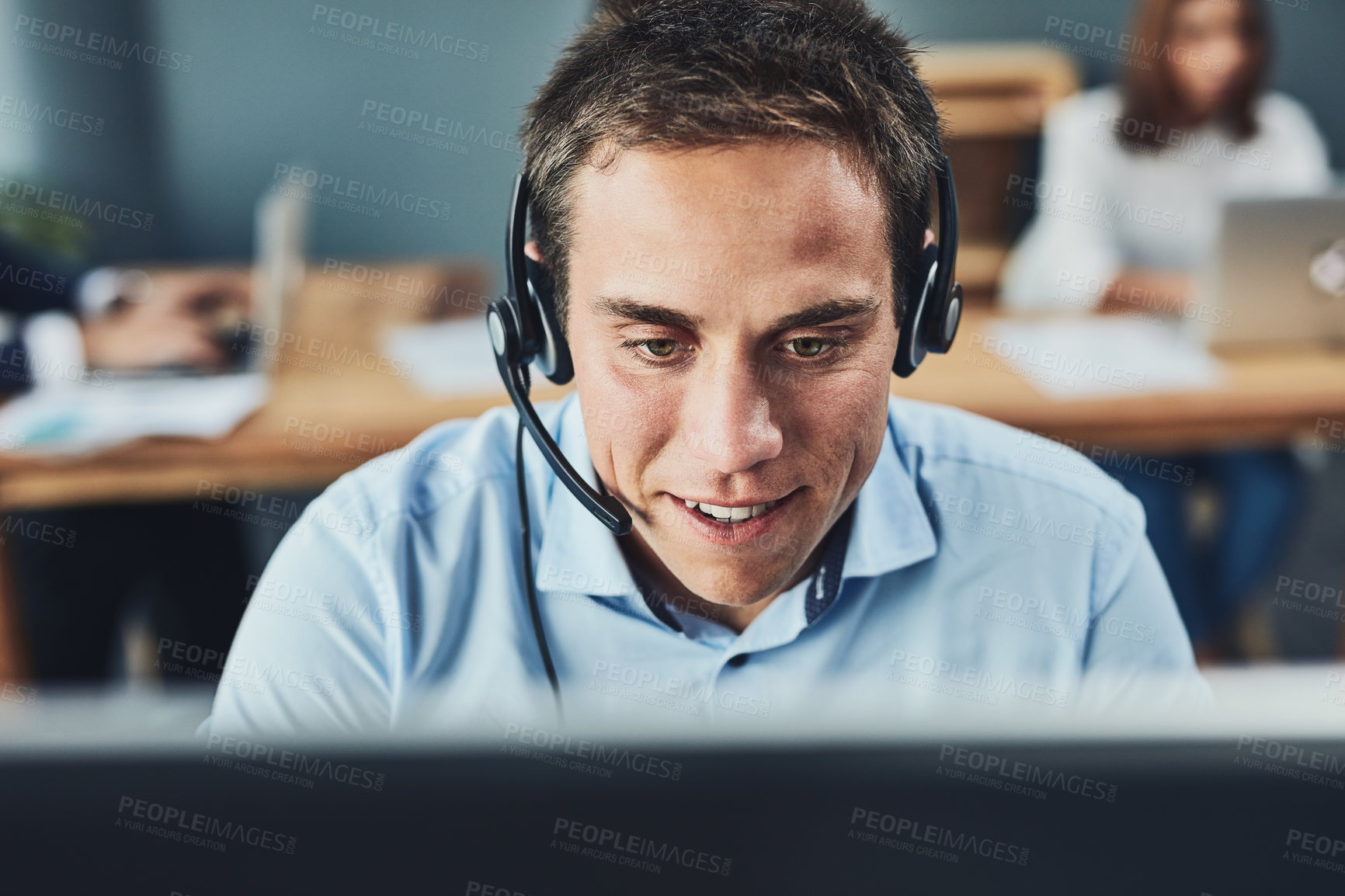 Buy stock photo Closeup of a young male call center agent consulting and giving support while working in a busy office. Face of a man and helpdesk worker or phone operator having a conversation