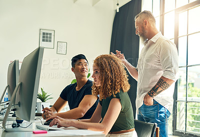 Buy stock photo Shot of two young creative businesspeople working on a computer in their office under the guidance of their manager