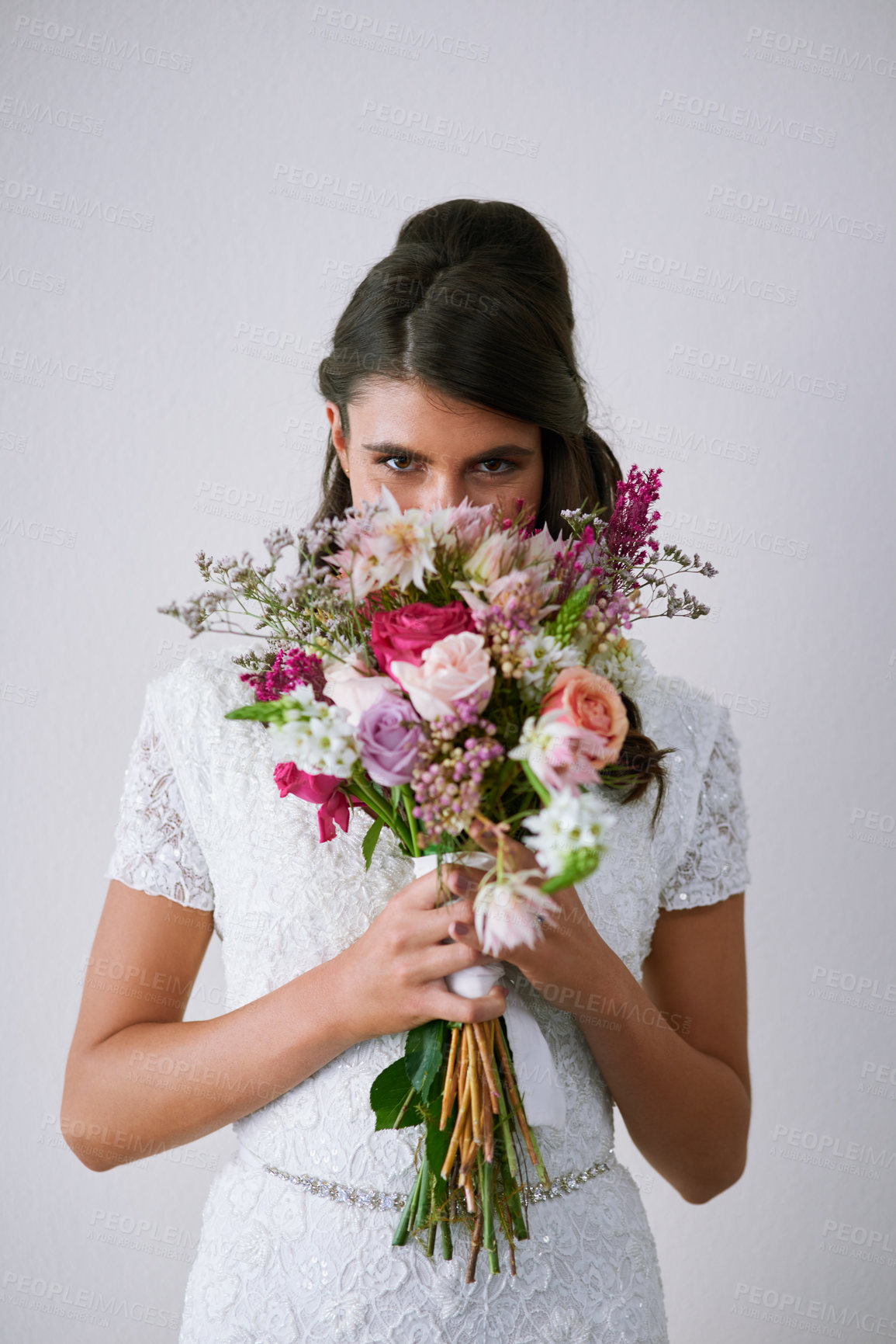 Buy stock photo Studio portrait of a young bride holding a bunch of flowers against a gray background