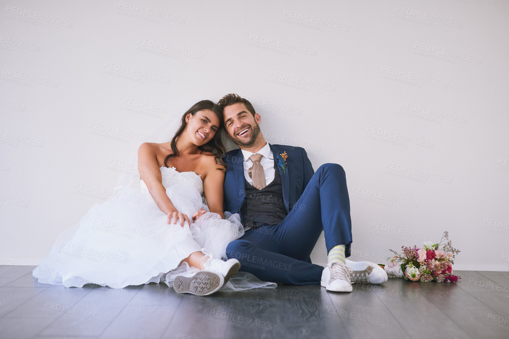 Buy stock photo Studio portrait of a newly married young couple sitting together on the floor against a gray background