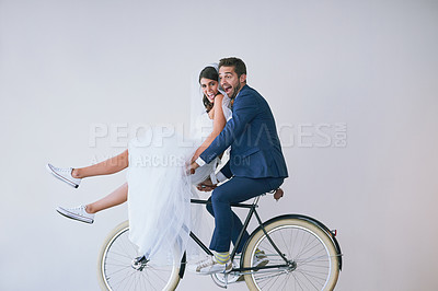Buy stock photo Studio portrait of a newly married young couple riding a bicycle together against a gray background