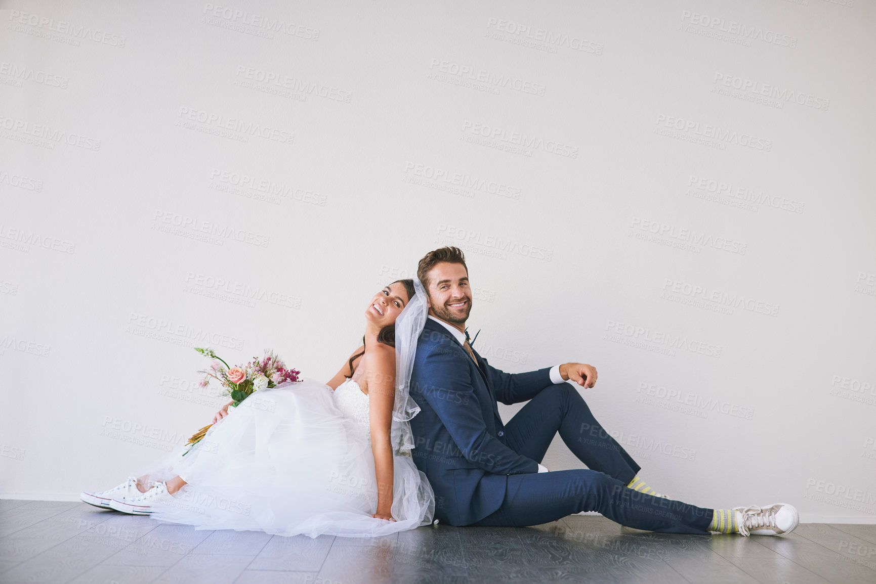 Buy stock photo Studio shot of a newly married young couple sitting back to back on the floor against a gray background